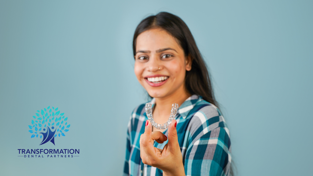 Smiling person holding clear dental aligners against a blue backdrop.
