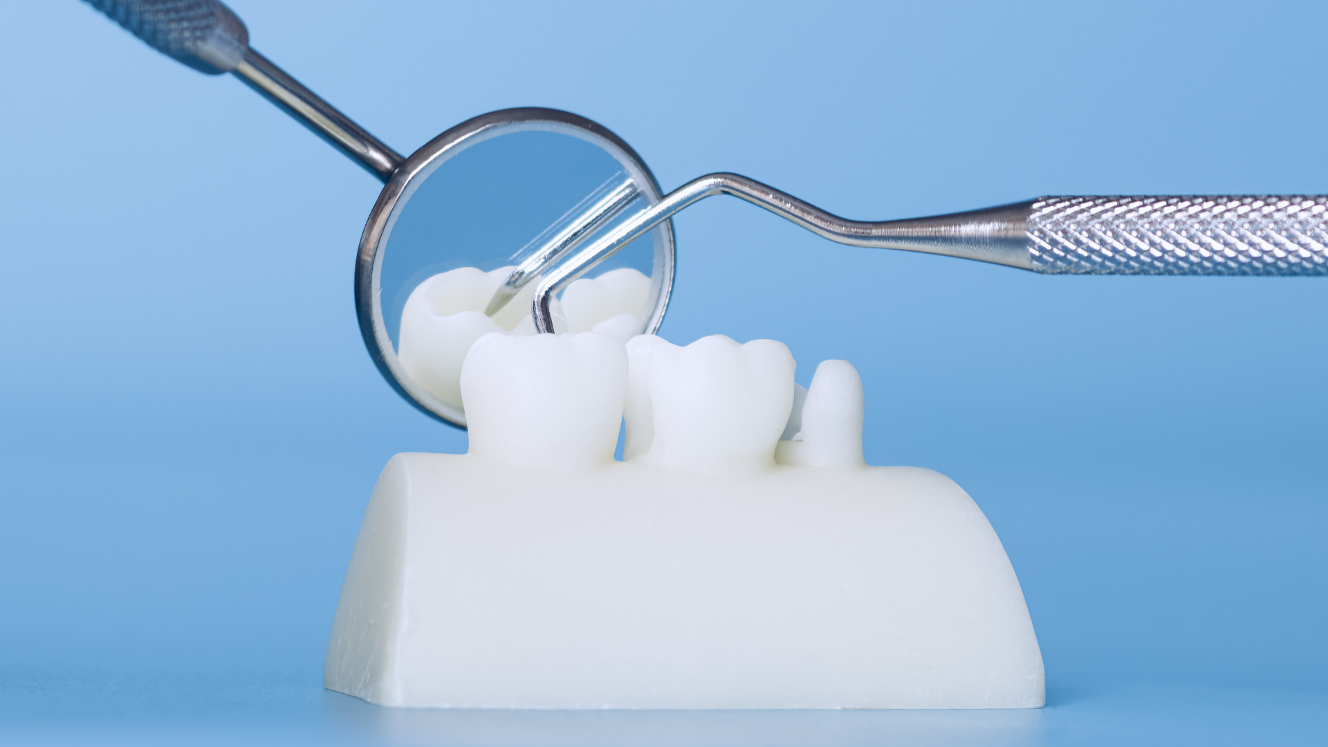 Dental tools examining a model set of teeth, reflecting in a dental mirror.