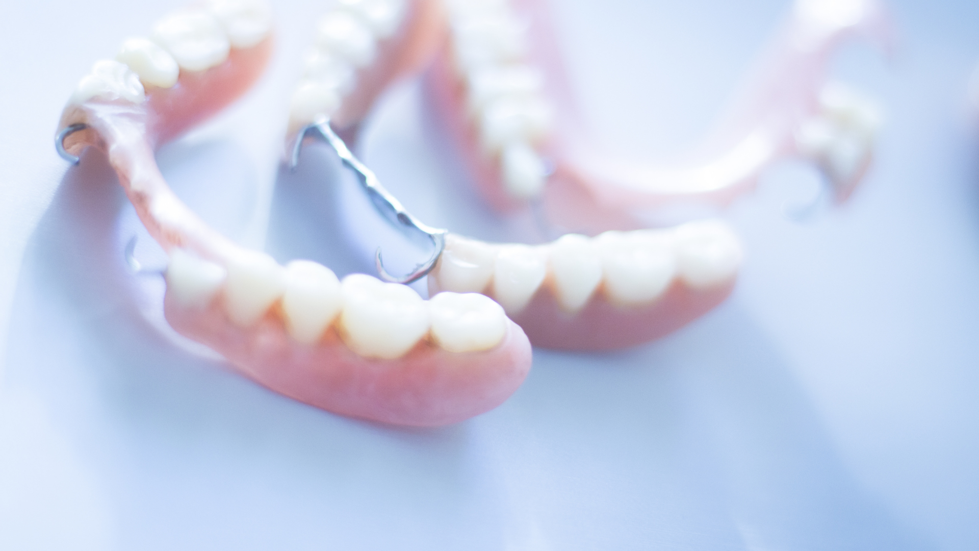 Close-up view of partial dentures on a light blue surface, showing pink gums and artificial teeth.