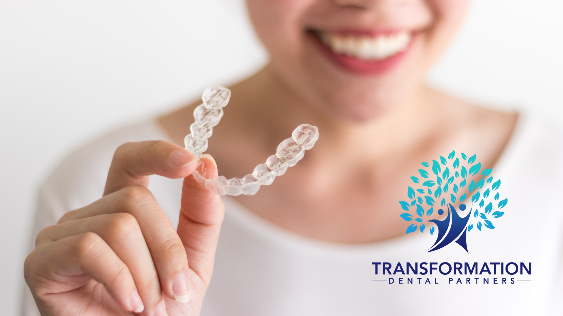 Woman holding clear dental aligner, smiling, Transformation Dental Partners logo.