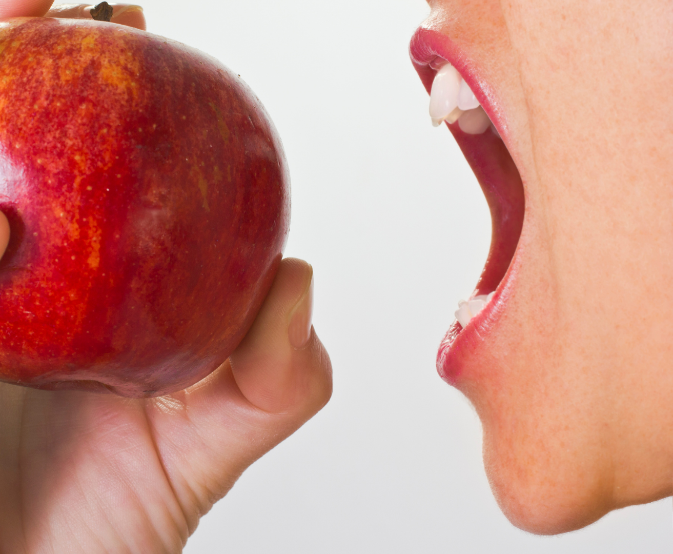 A woman is biting into a red apple with her mouth open