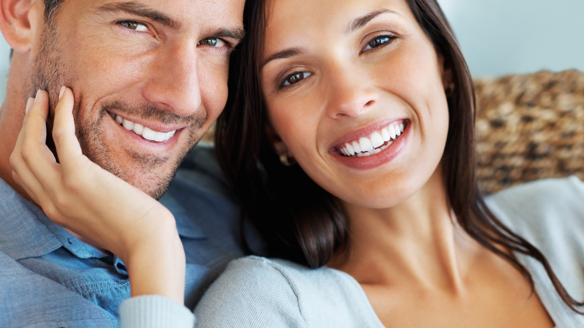 A man and a woman are smiling for the camera while sitting on a couch.