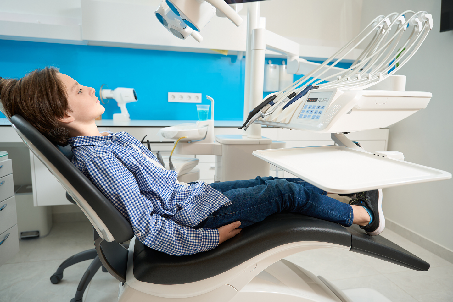 A young boy is laying in a dental chair with his eyes closed.