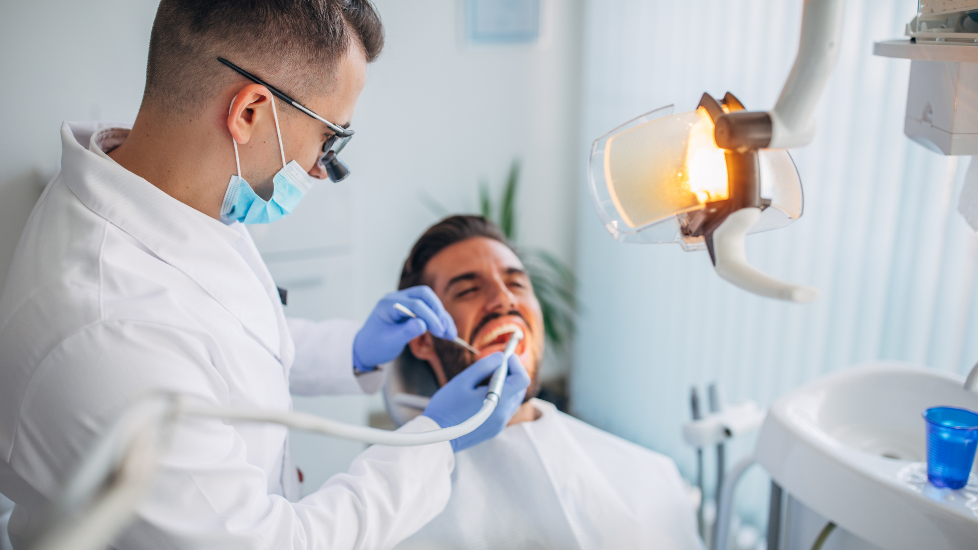 Dentist examining a patient with a mouth mirror in a bright clinic, with a dental light overhead