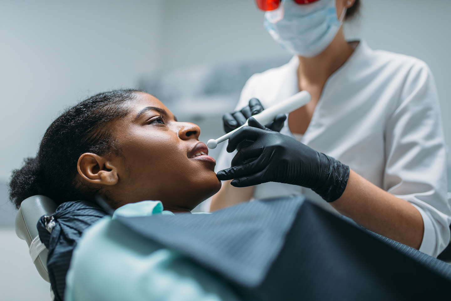 A woman is sitting in a dental chair getting her teeth examined by a dentist.