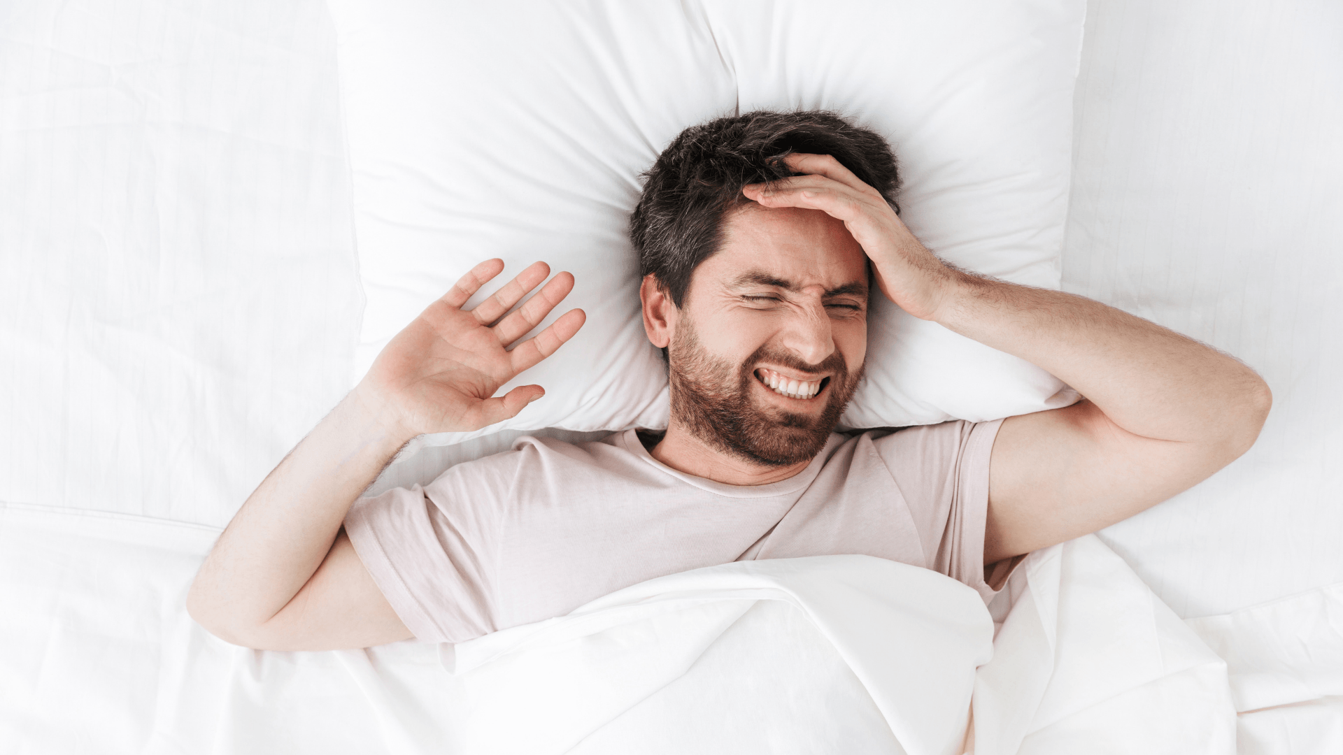 A man is laying in bed with his hand on his head.