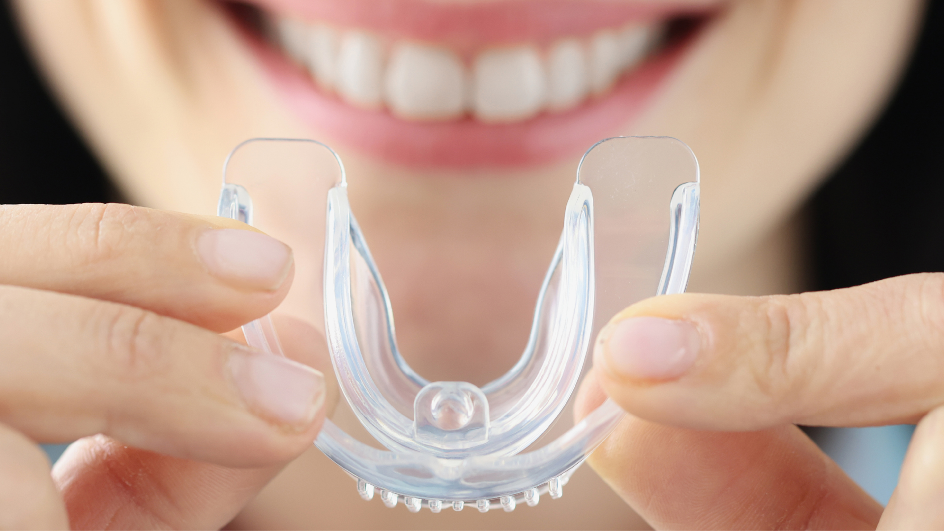 A woman is holding a mouth guard in front of her mouth.