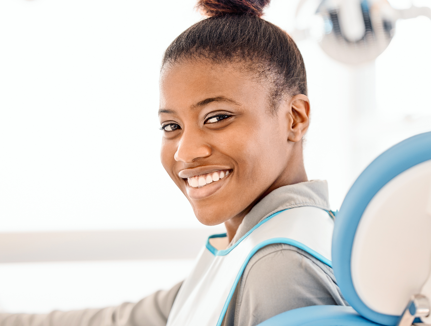 A woman is smiling while sitting in a dental chair.