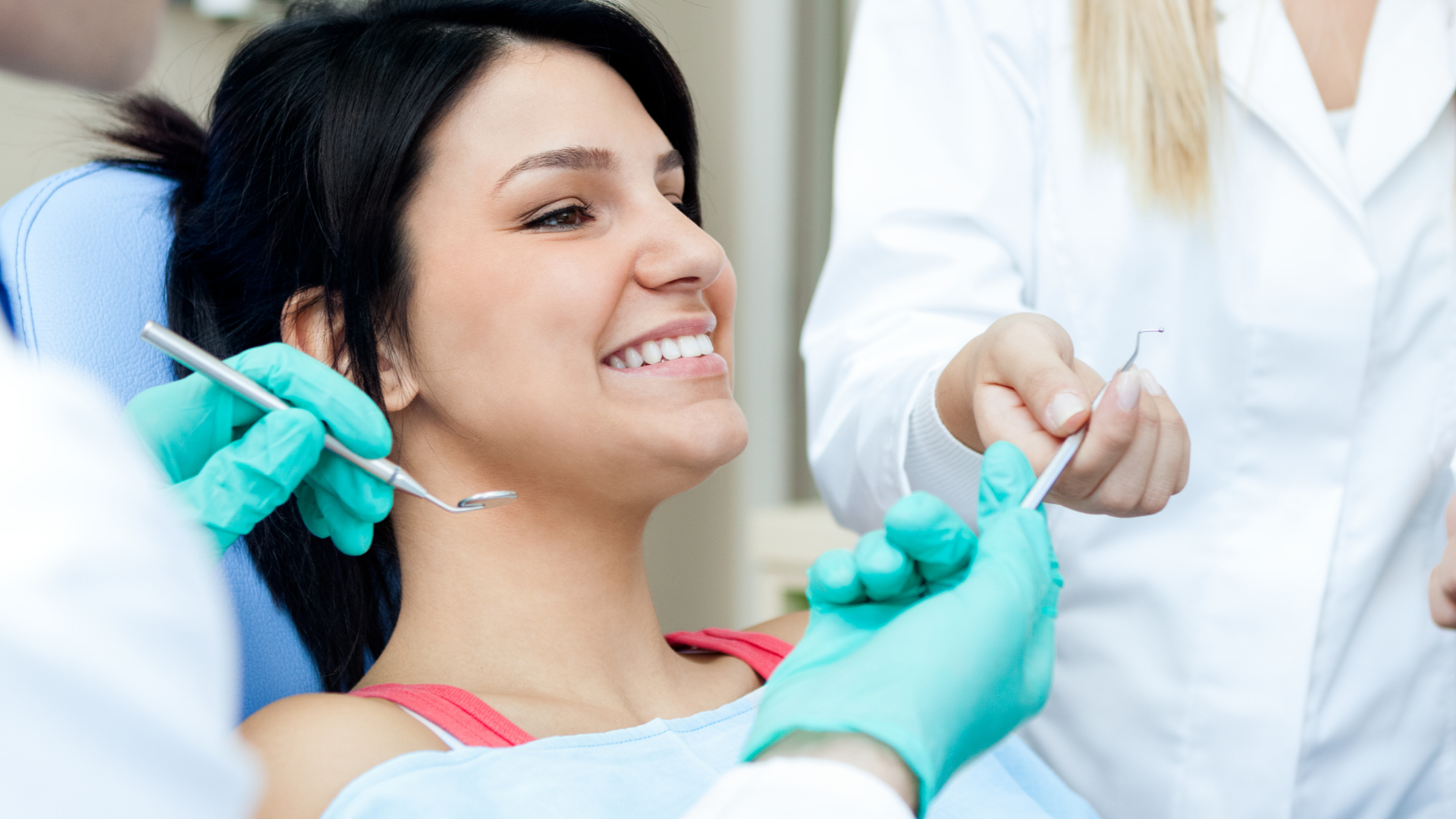 A woman is sitting in a dental chair while a dentist examines her teeth.