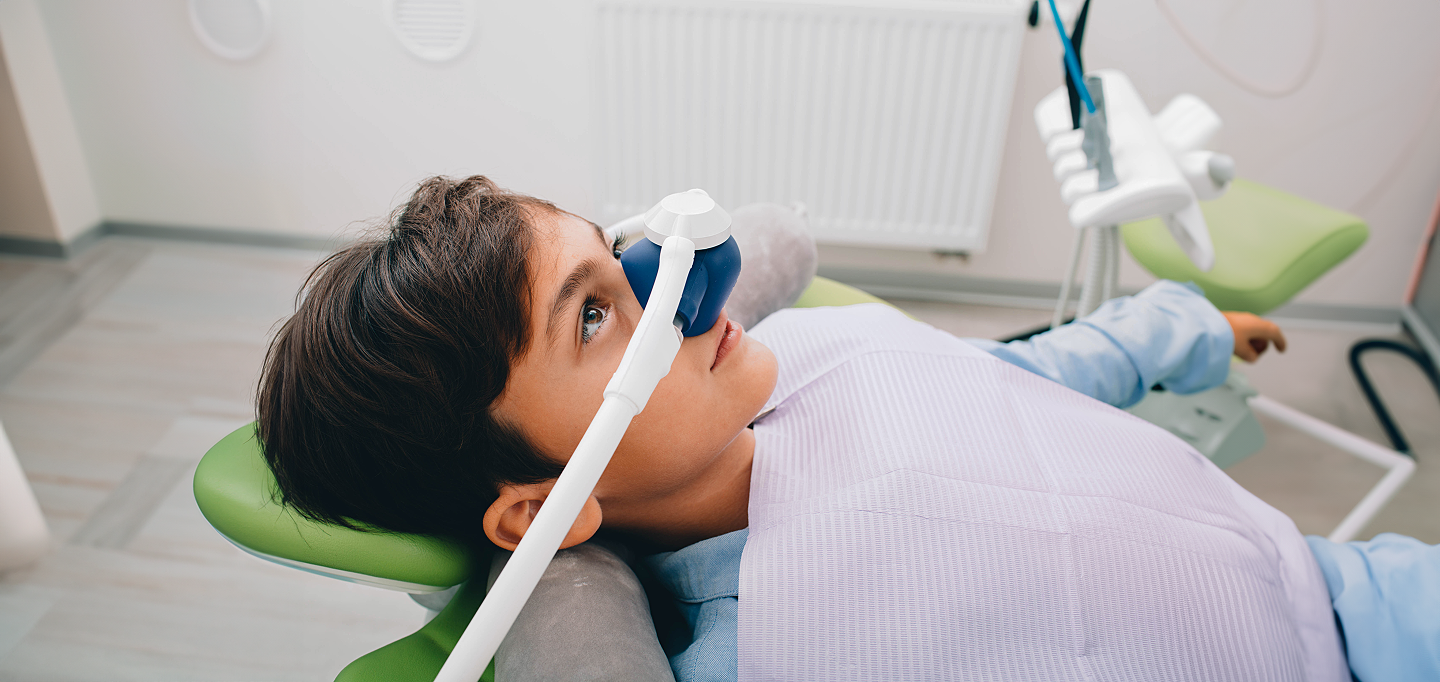 A young boy is laying in a dental chair with an oxygen mask on his face.