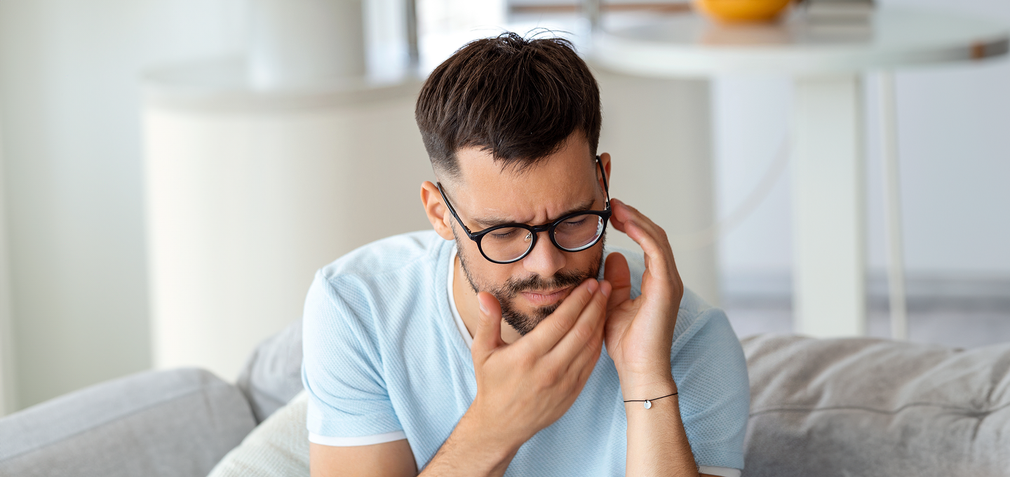A man wearing glasses is sitting on a couch with his hands on his face.