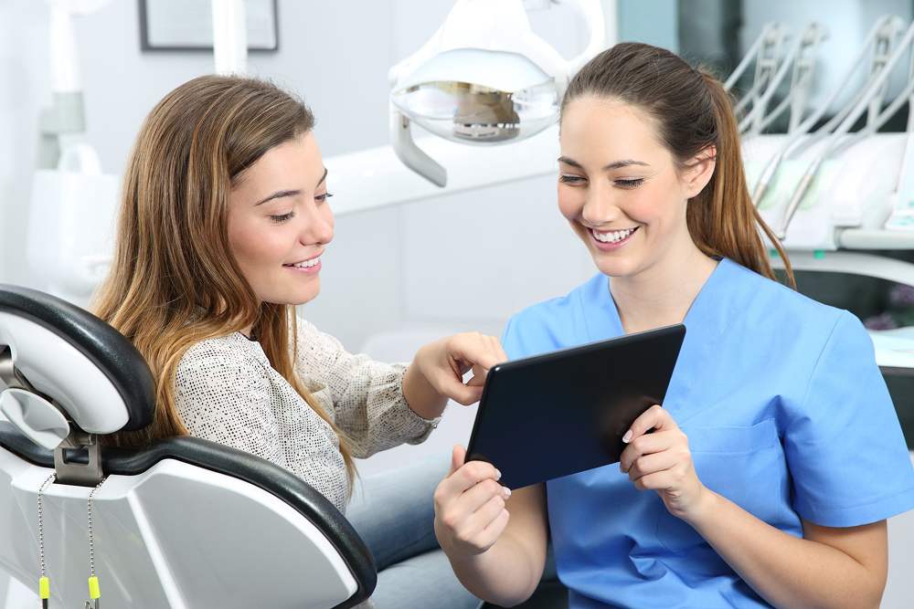 A dentist is showing a tablet to a patient in a dental chair.