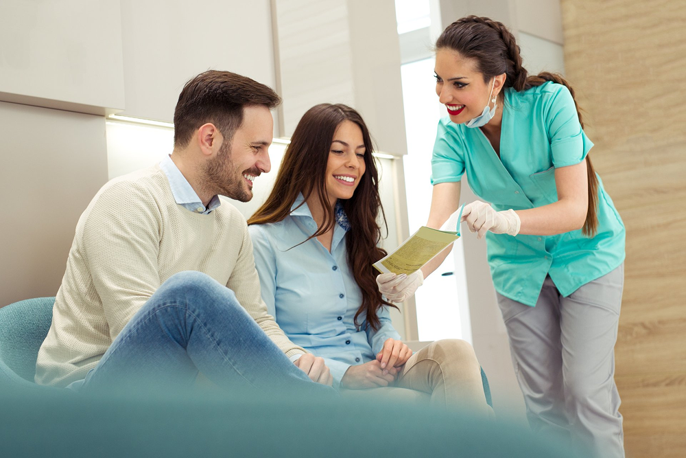 A man and a woman are sitting on a couch talking to a dentist.