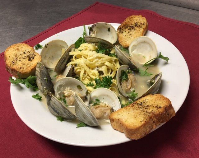 A white plate topped with clams noodles and garlic bread