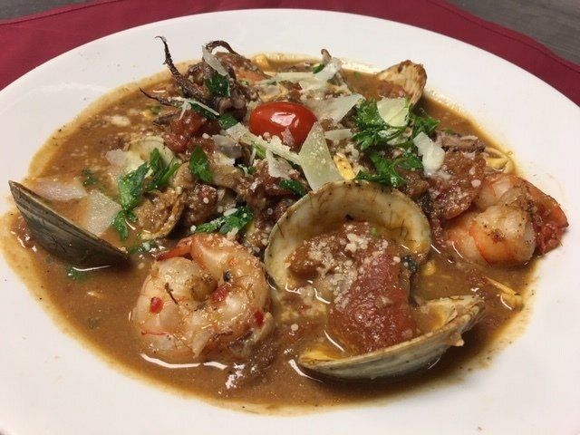 A white plate topped with a stew of shrimp clams and meat.