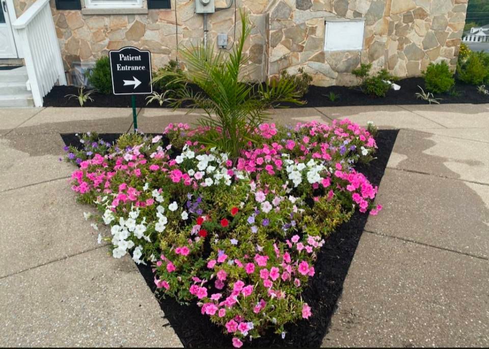A triangular garden bed filled with pink and white flowers and a palm tree, next to a sign pointing to private entrance.