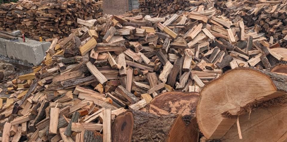 A large pile of split firewood with textured logs in the foreground and stacked wood in the background.