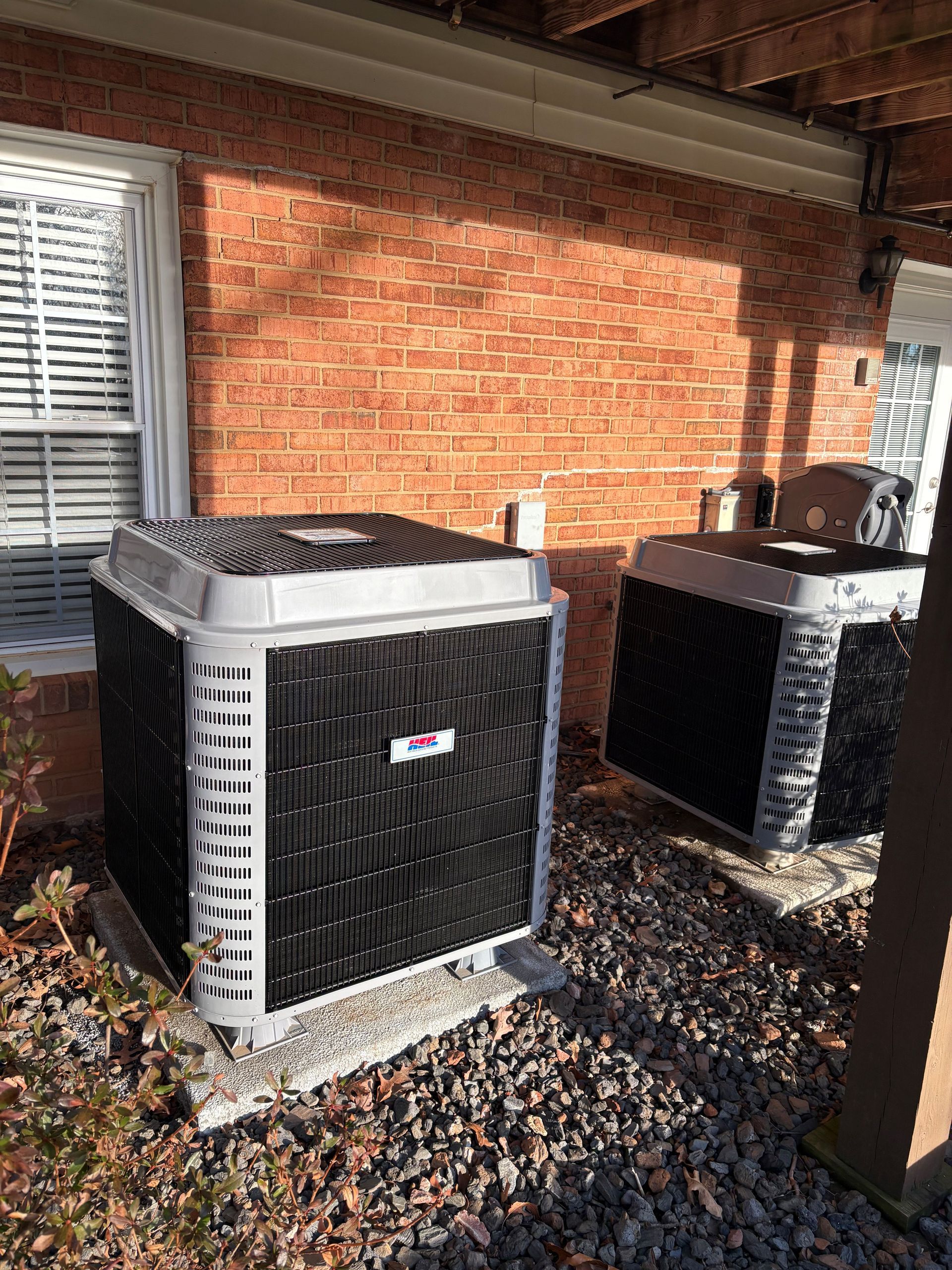 HVAC technician in yellow hard hat giving thumbs up next to air conditioning unit.