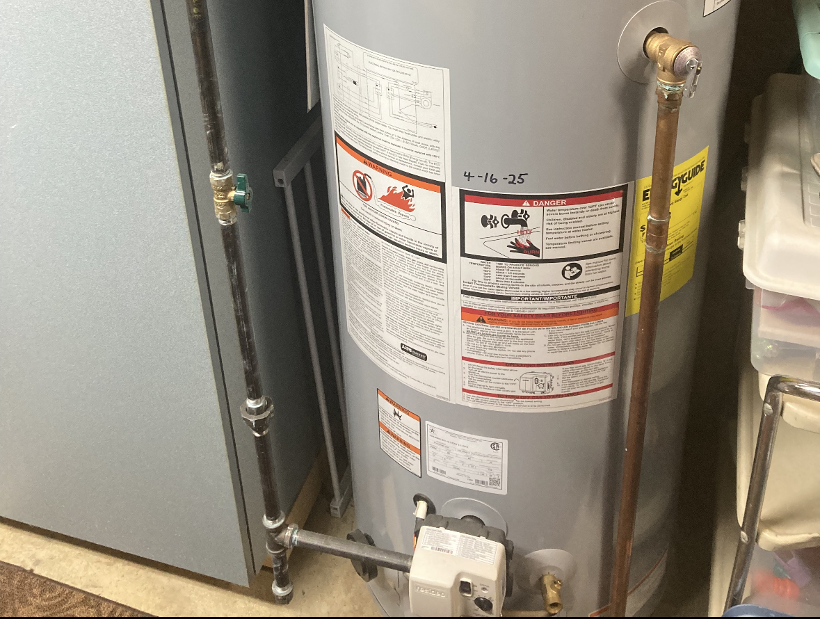 Plumber connecting pipes to a white water heater, indoors. Plumber working on a hot water heater, connecting pipes.