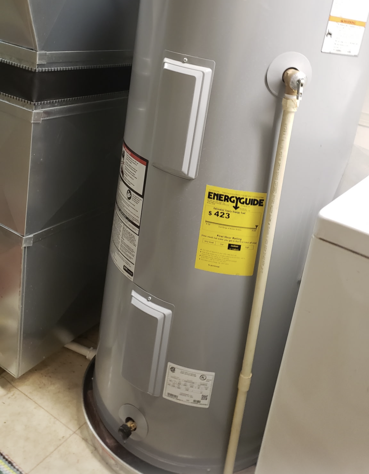Woman in striped shirt checks phone near a water heater in a utility room.