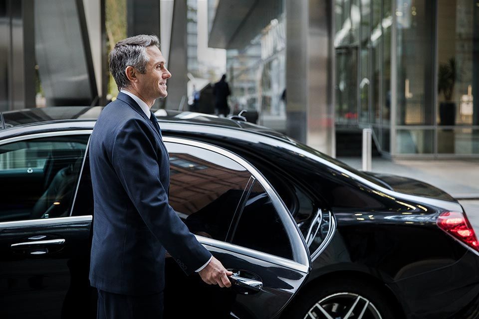 A man in a suit is opening the door of a black car.
