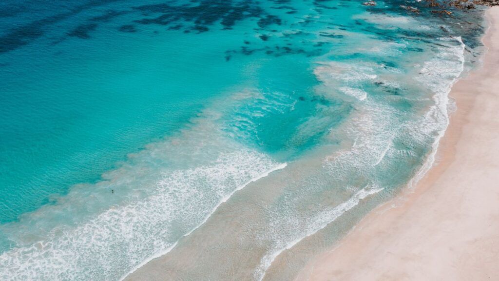 Turquoise water gently waves onto a white sandy beach.