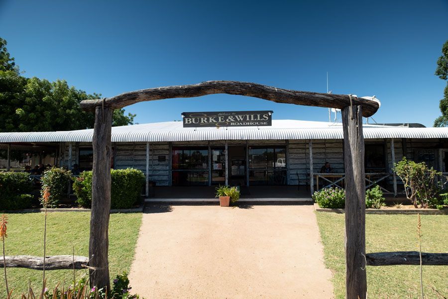 Burke & Wills winery entrance under a wooden arch, green lawn, clear blue sky.