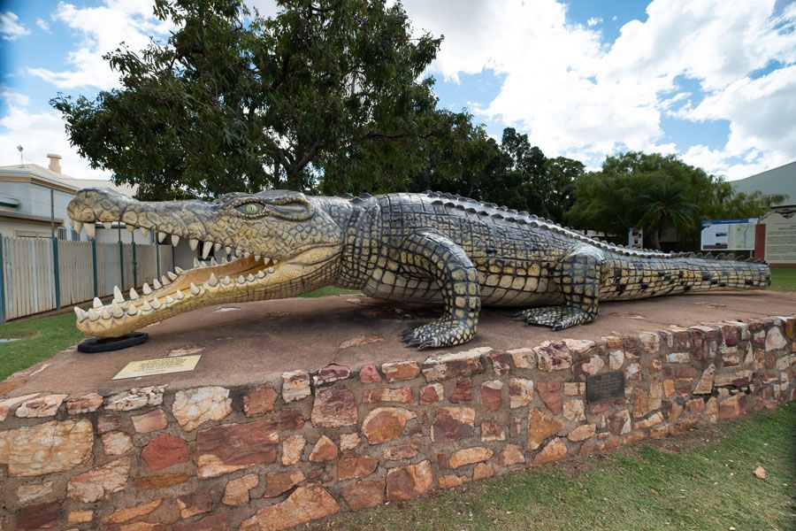 Giant crocodile sculpture on a brick base in front of a building and trees.