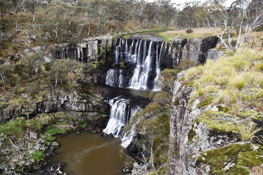 Waterfall cascading down rock formations, surrounded by trees and vegetation.