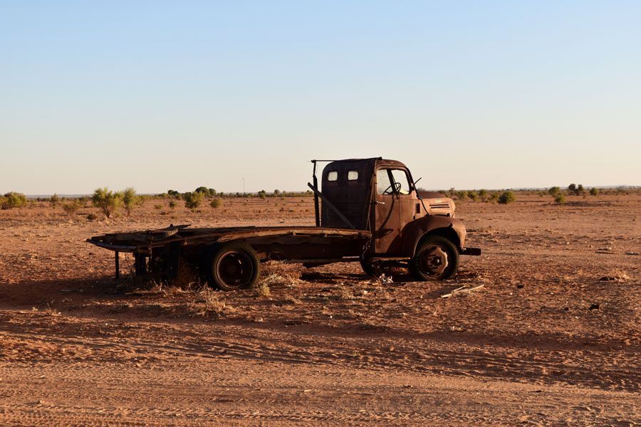 Rusty, abandoned flatbed truck in a dry, barren landscape under a clear sky.