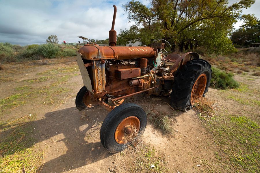 Rusty, abandoned tractor in a field with dry vegetation and a cloudy sky.
