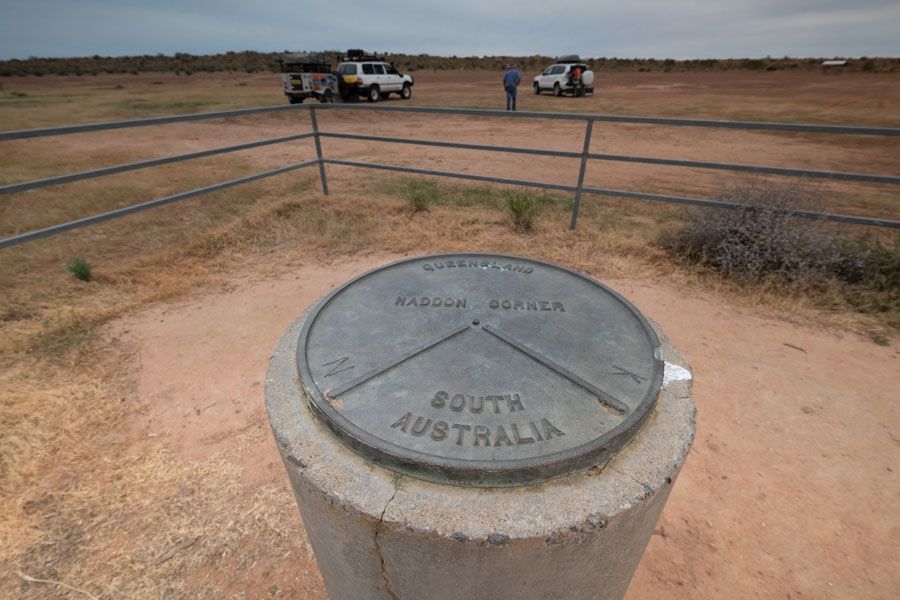 Marker stone for the South Australia border with vehicles and people in the background.