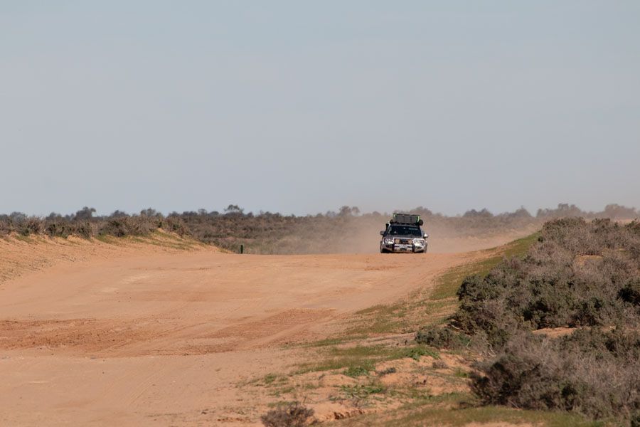 SUV driving on a dirt road in a dry, sandy landscape, kicking up dust.