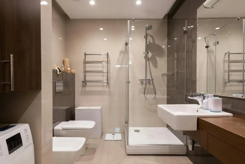 Modern bathroom with shower, toilet, sink, and washer. Neutral tones, chrome fixtures.