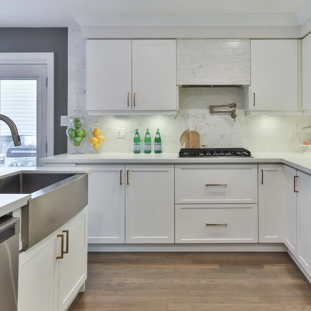 Modern white kitchen with stainless steel appliances, marble backsplash, and wooden floors.