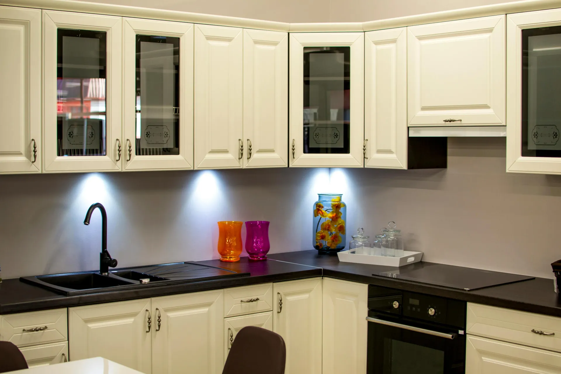 White kitchen cabinets with black countertops and black sink. Under-cabinet lighting illuminates the space.