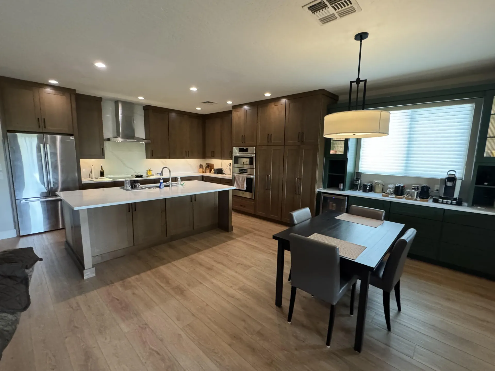 Modern kitchen with wooden cabinets, stainless steel appliances, island, dining table, and light wood floors.