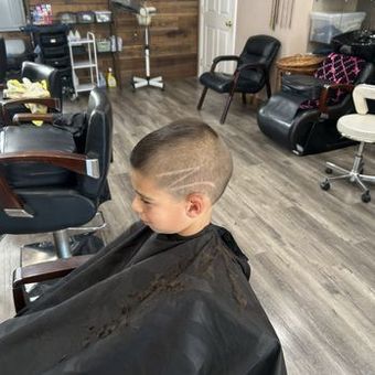 A young boy getting a haircut in a barbershop. He has a design shaved into his hair.