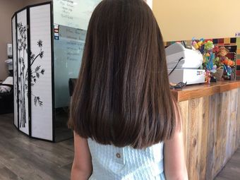 A young girl has her hair styled by someone wearing a black apron in a salon.