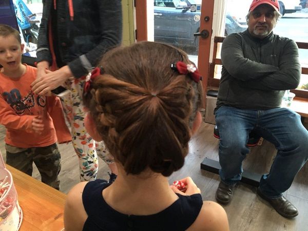 Boy with curly hair smiles brightly, standing in a salon while a woman brushes his hair.