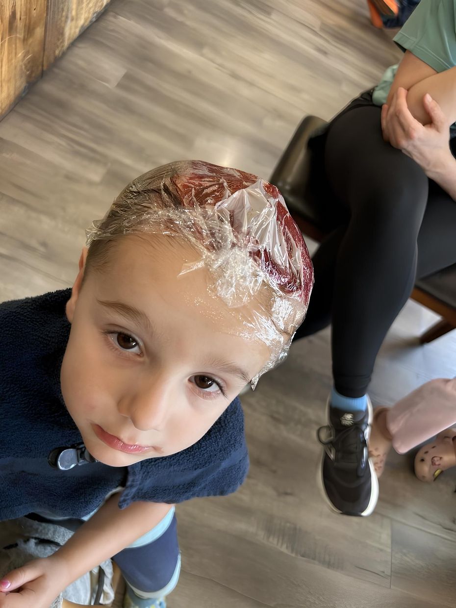 Young girl with pink and blue hair, smiling in a salon, wearing overalls and a white shirt.