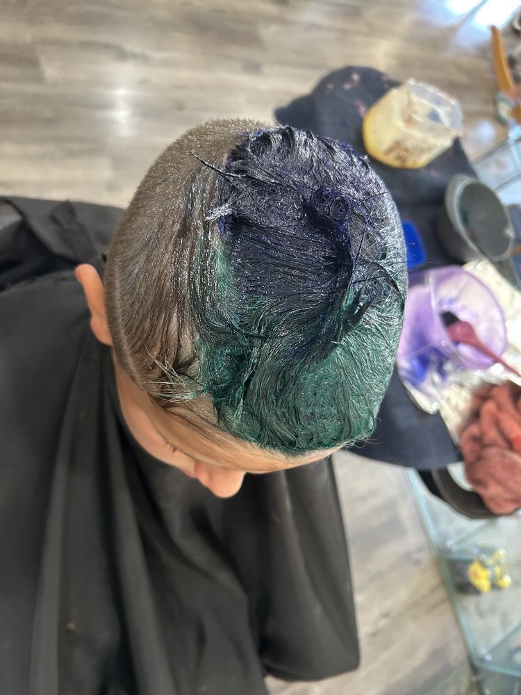 Colorful bottles and hair chalk on a vanity, reflecting in a mirror.