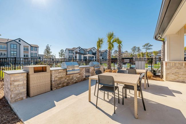 Outdoor grilling area with a table and chairs, next to brick and stone barbecue structures and palm 