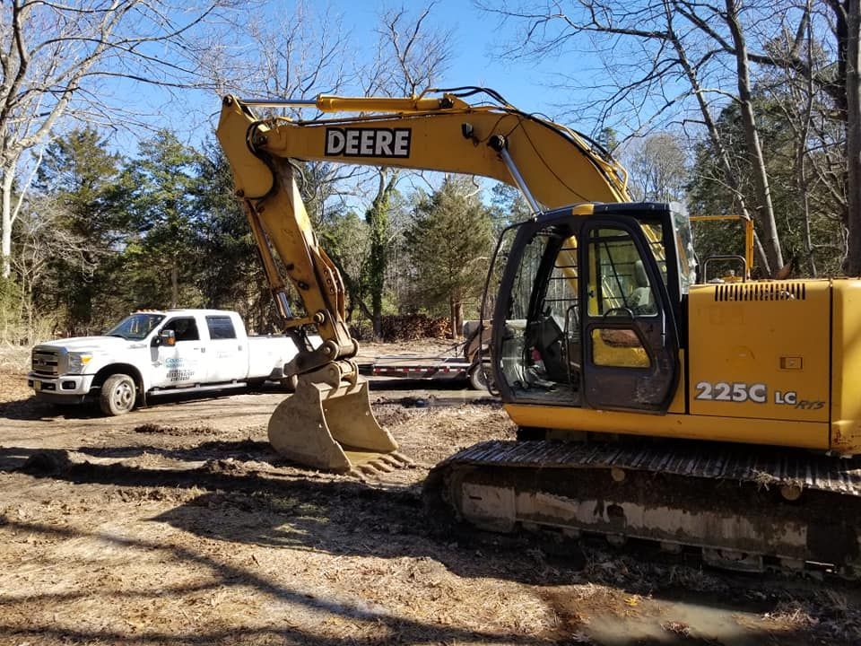 A yellow deere excavator is parked next to a white truck.