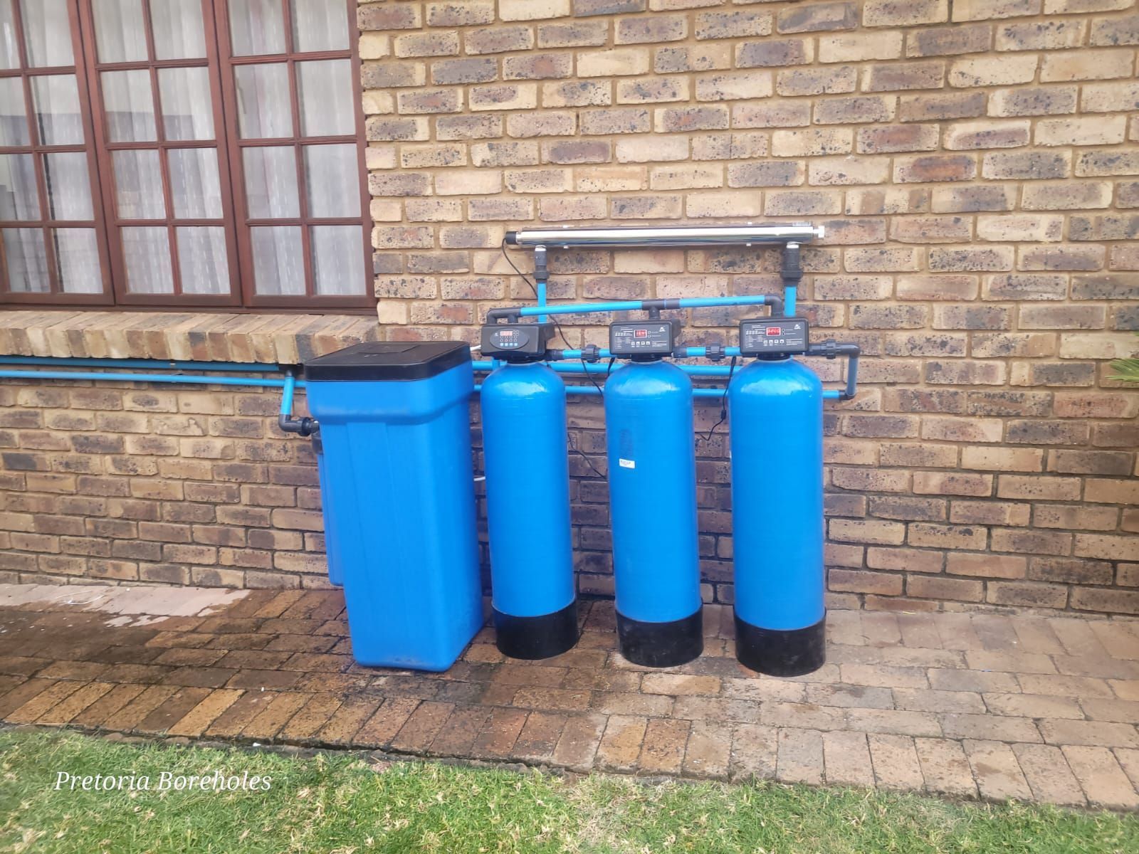 Three blue tanks are sitting in front of a brick wall.