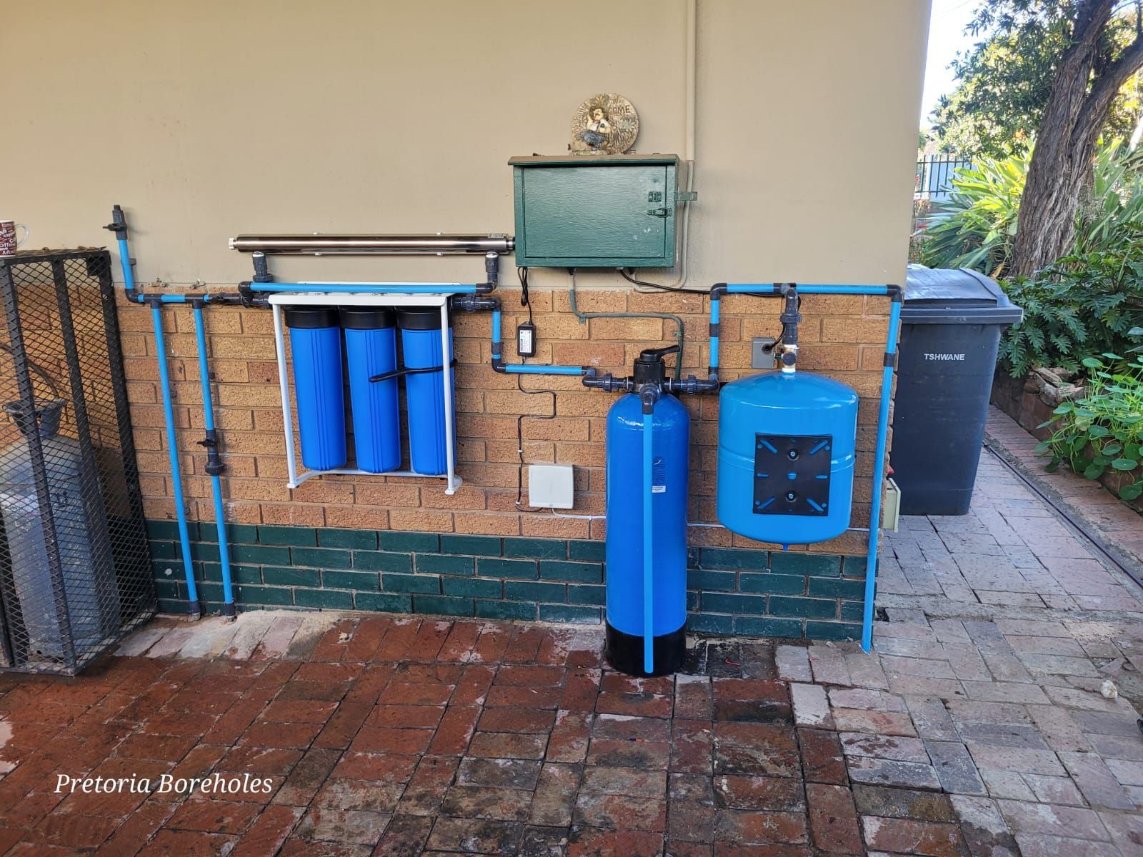A blue water filter is installed on the side of a building