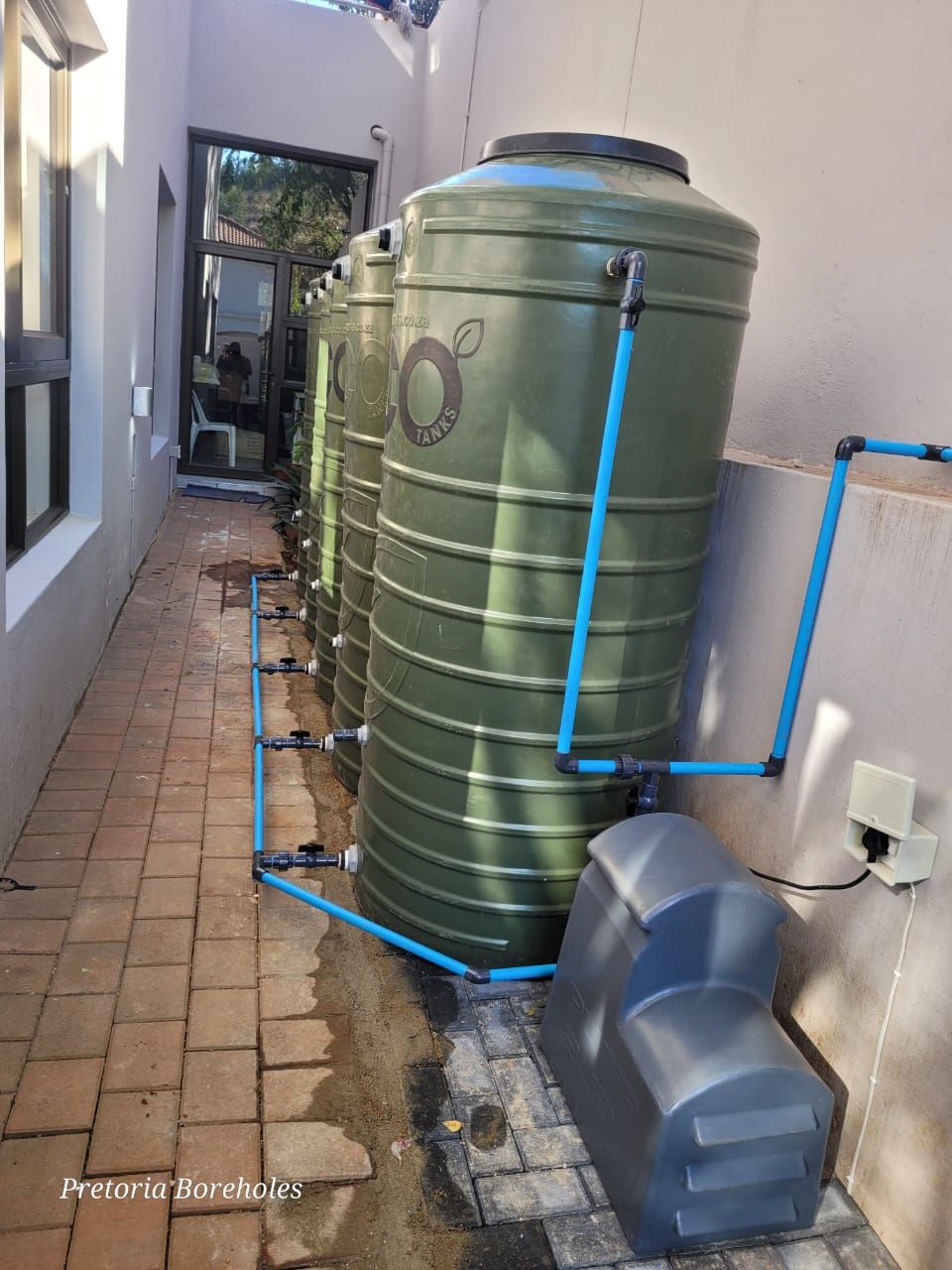 A row of green water tanks sitting next to each other on a sidewalk.