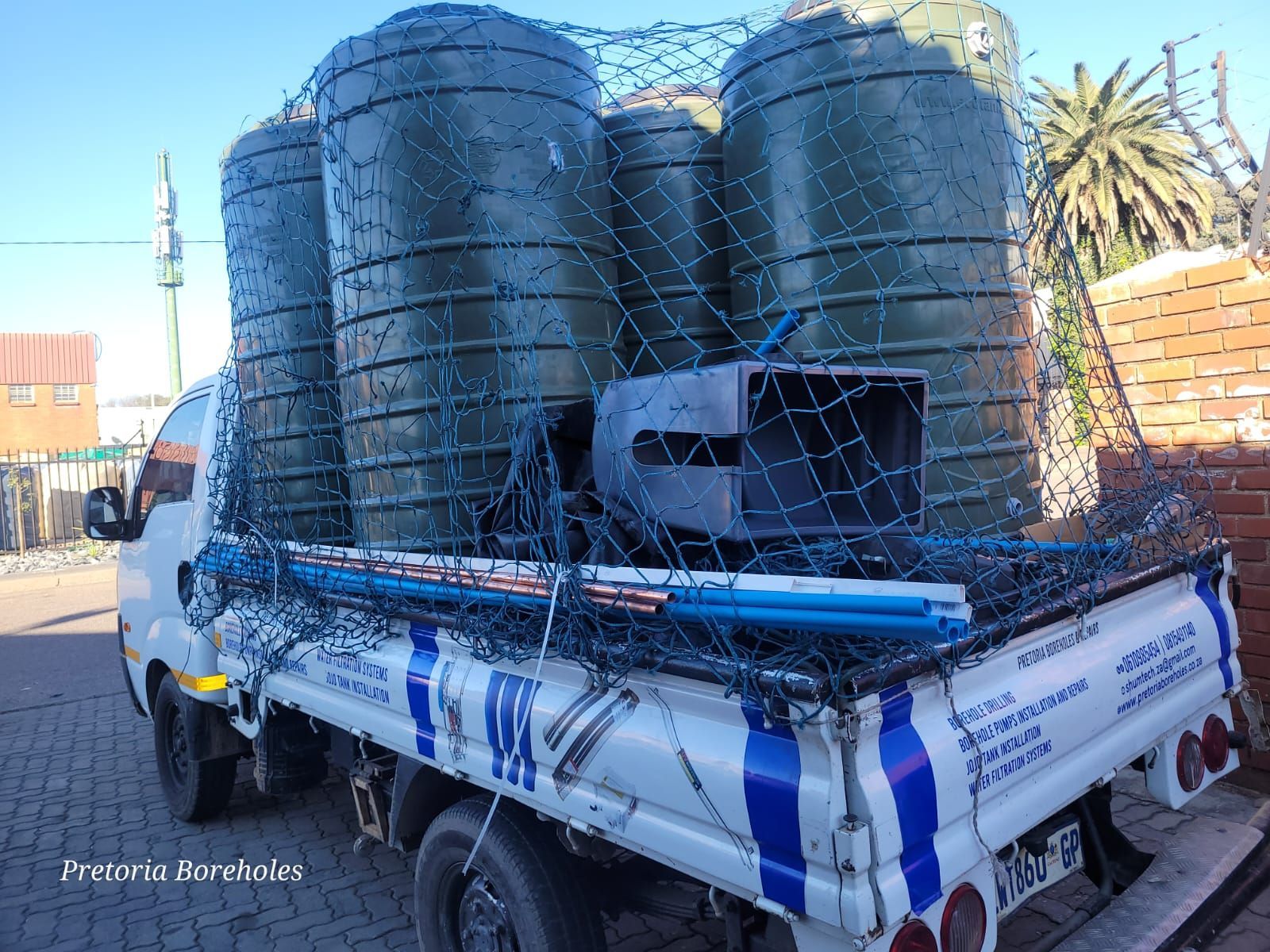 A white truck with a net on the back is loaded with water tanks.