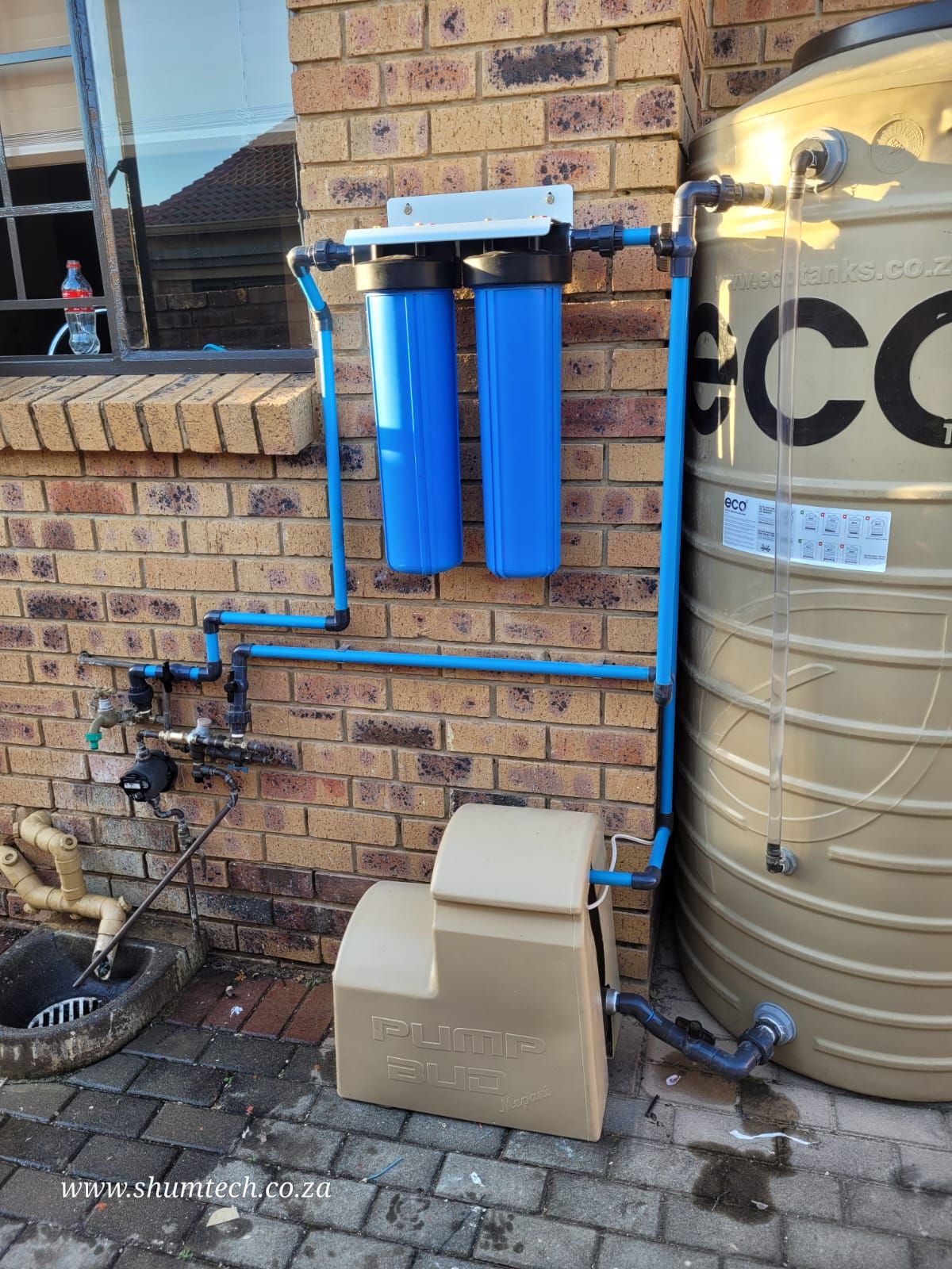 A water tank and filters is sitting next to a brick wall.