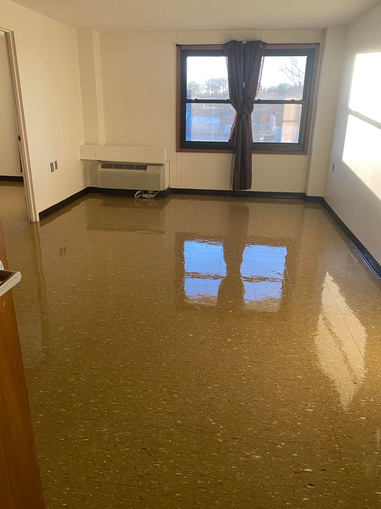 An empty living room with a shiny floor and a window.